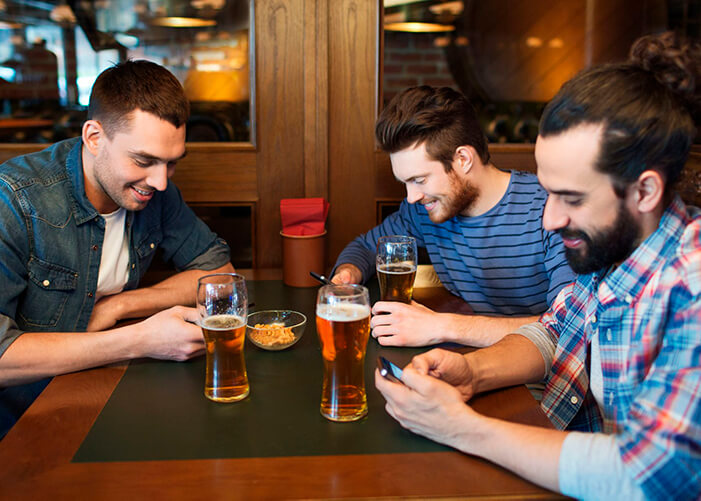 Amigos sentados na mesa do bar, cada um mexendo no seu celular