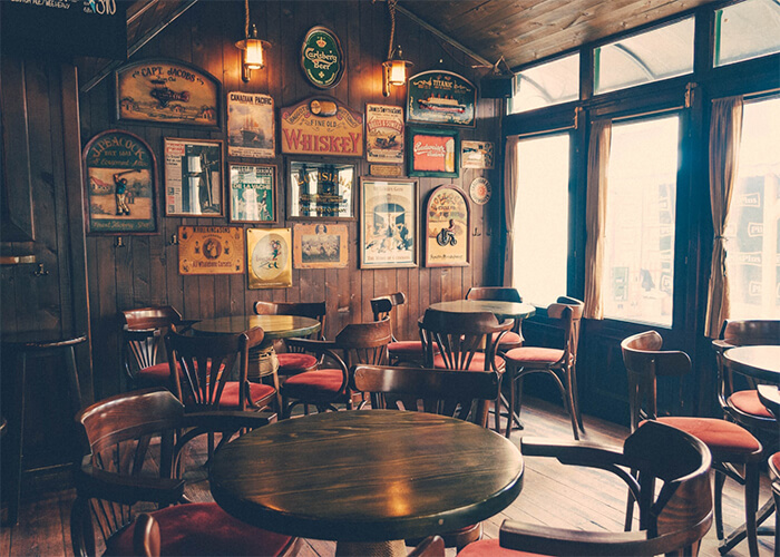 Foto interna de restaurante com mesas redondas, janelas grandes e parede com quadros no estilo texas