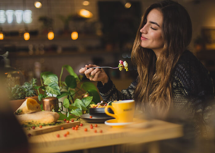 Mulher em um restaurante comendo macarrão com um semblante tranquilo e sensação de satisfação